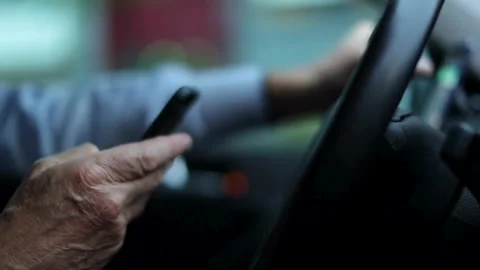 Close-up of old man hand holding a phone and steering wheel of a car while Stock-Footage 336265937
