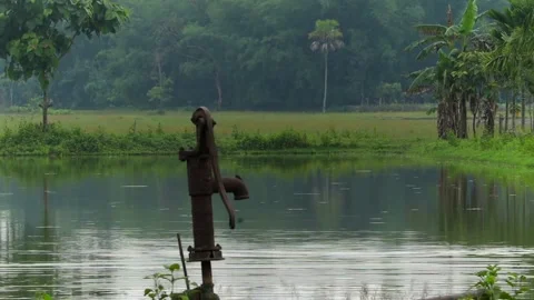 Close-Up of Old Rusty Hand Pump Beside a Peaceful Village Pond Stock-Footage 336531422