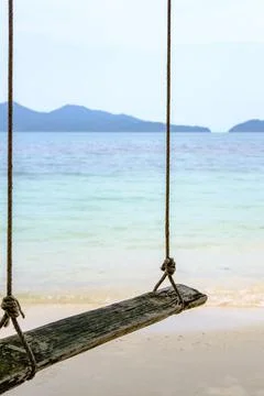 Close up, old swing hanging on a tree on sandy beach, blue sea and sky backgr Stock-Fotos