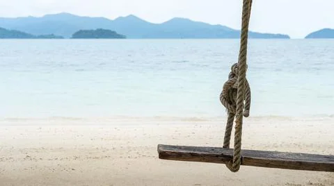 Close up, old swing hanging on a tree on sandy beach, blue sea and sky backgr Stock Photos