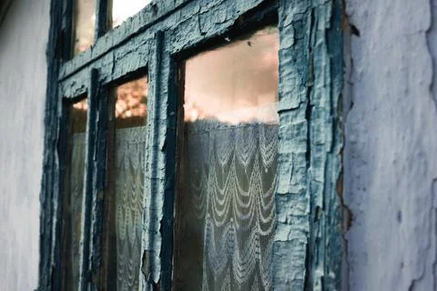 Close-up of an old weathered window with peeling paint and lace curtain in .. Stock Photos
