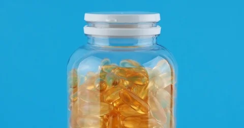 Close-up Omega 3 orange capsules transparent bottle rotate blue background Stock Footage 126336645