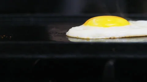 Close up one egg fried on a black griddle with smoke Stock Footage 246553574