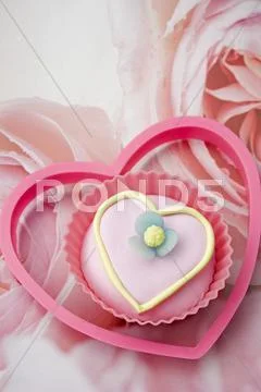 Close Up Of One Pink Iced, Love Heart Shaped Cup Cake With A Pink Plastic Heart