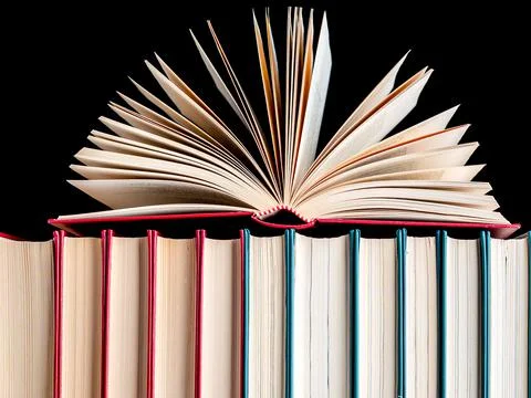 Close-up of an open book on a row of hardback books against a dark background Stock Photos