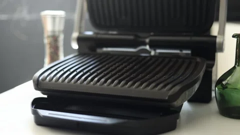 Close-up of an open electric grill with a green bottle and pepper grinder Vidéo 342280576