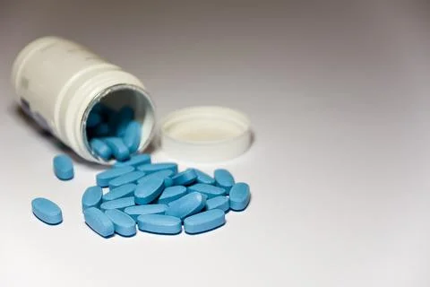 Close up of open plastic bottle with scattered many blue erection pills on wh Stock Photos
