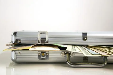 A close-up of an open silver aluminum case with cash spilling out from inside Stock Photos