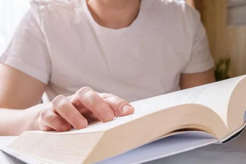 Close-up of opened thick paper book in hands of woman in white T-shirt Stock Photos