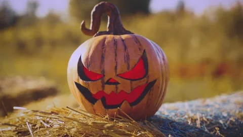Close-up orange carved pumpkin evil Jack o Lantern lying on stack of straw Video stock 318181352