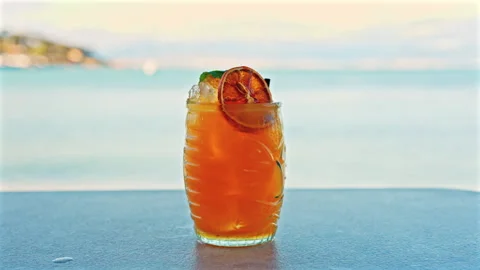 Close up of an orange cocktail on a table with a blurred view of the sea on the Stock Footage 308759114