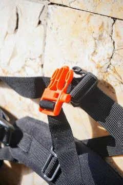 Close up of an orange whistle and orange plastic buckle on a black backpack Photos