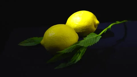 Close up orbiting footage of vibrant lemons and peppermint leaves on black Stock Footage 314500365