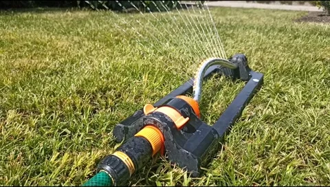 Close up of an oscillating lawn sprinkler spraying water on fresh green grass Stock Footage 339171879