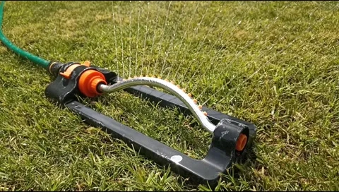 Close up of an oscillating lawn sprinkler spraying water on fresh green grass Stock Footage 339171901