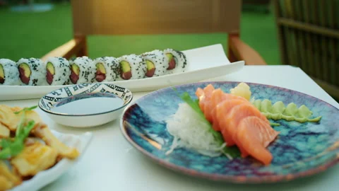Close-up of an outdoor dining table set with sushi rolls, tempura and salmon 库存影片 344793325