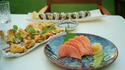 Close-up of an outdoor dining table set with sushi rolls, tempura and salmon Stock Footage 344793559