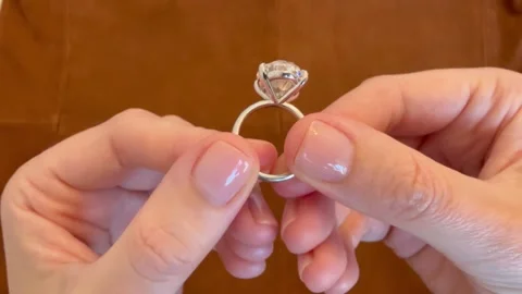 Close up of oval diamond platinum ring shown between hands on suede background Stock Footage 316748443