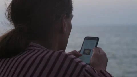 Close up over the shoulder view of man scrolling newsfeed on defocused sea Stock Footage 133862373