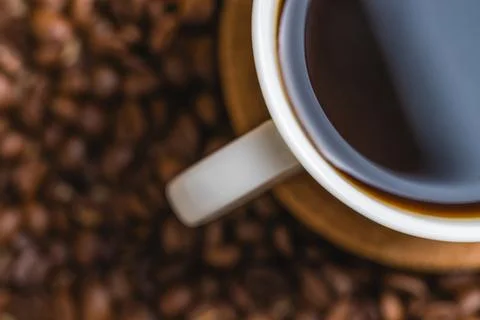 Close-up overhead view of black coffee surrounded by roasted beans Stock Photos