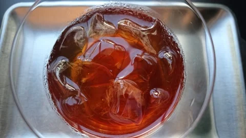 Close-up overhead view of iced dark tea in clear glass on metal tray Stock Footage 344747737
