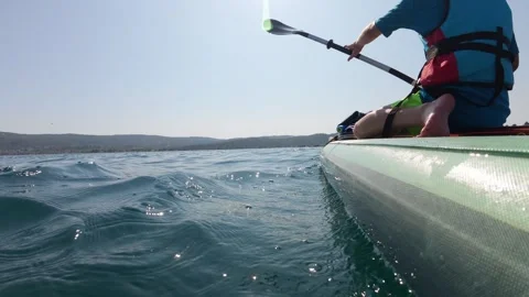 Close-up of a paddle lifting water while a child paddles on a SUP board. Dynamic 스톡 동영상 313808827