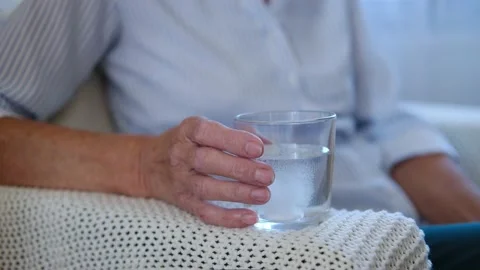 Close up painkiller tablet dissolves in glass on table in hand elderly woman Stock Footage 158064532