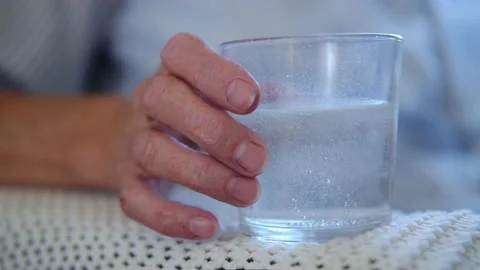 Close up painkiller tablet dissolves in glass on table in hand elderly woman Video stock 160455651