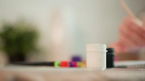 Close up of paint jars and brush in soft focus with colorful background objects Stock Footage 347224173