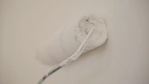 A close-up of a paint roller applying fresh white paint to a wall. The texture Stock Footage 303814226