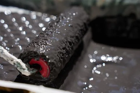 Close up of paint roller covered with dark paint inside tray. Concept of ro.. Fotos de archivo