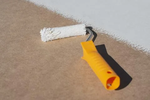 Close-up a paint roller with a yellow handle applying a smooth layer of white Photos