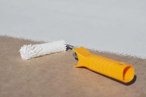 Close-up a paint roller with a yellow handle applying a smooth layer of white Photos