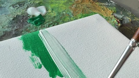 A close-up of a paintbrush applying green paint to a canvas. 스톡 동영상 343300849