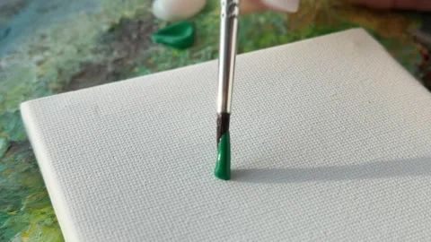 A close-up of a paintbrush dipped in green paint on a canvas. 스톡 동영상 343300787