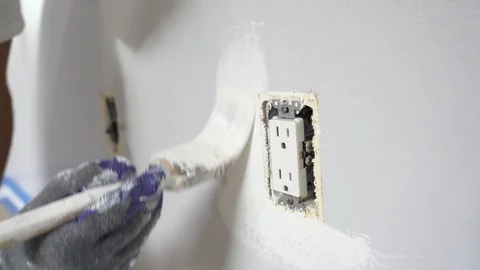 Close up of painter hands with gloves painting the wall around power outlet. 4k Stock Footage 129140341