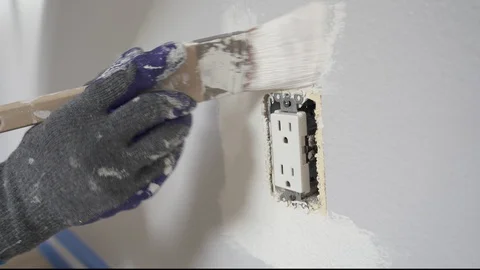 Close up of painter hands with gloves painting the wall around power outlet. 4k Stock Footage 129140391