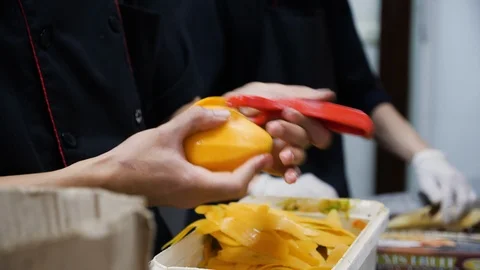 Close up of pair of hands peeling mangos with peeler in vietnamese restaurant Stock Footage 147349086