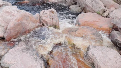 Close Up/Pan Left-Bubbling Waves Flowing Over White And Pink Rocks In Stream in Stock Footage 107014161