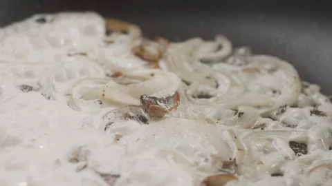 Close-up on pan preparing onion with champignons poured with cream Stock Footage 123899116