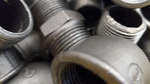 Close-up pan shot of a pile of black malleable cast iron pipe fittings and threa Stock Footage 336484589