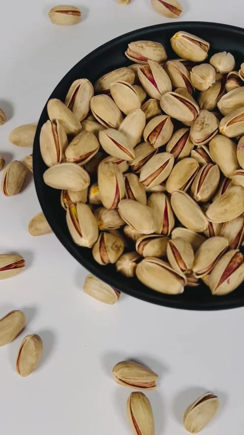 Close-up pan shot from right to left of roasted pistachios on a black plate Vídeos de archivo 336136141