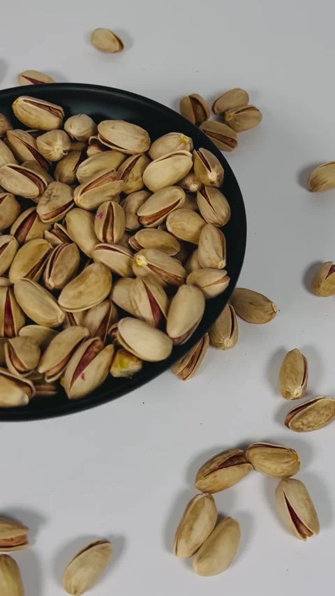 Close-up pan shot from right to left of roasted pistachios on a black plate Vídeos de archivo 336136142