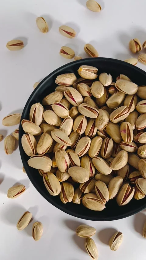 Close-up pan shot from right to left of roasted pistachios on a black plate Vídeos de archivo 336136144