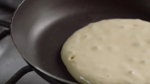 Close-up of Pancake Batter Cooking in Black Frying Pan with Small Bubbles on Stock Footage 343708769