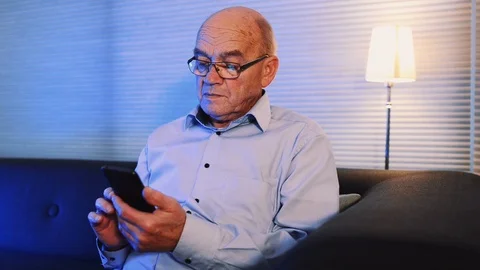 Close up panning shot of senior man playing with his mobile phone at home Stock Footage 99014446