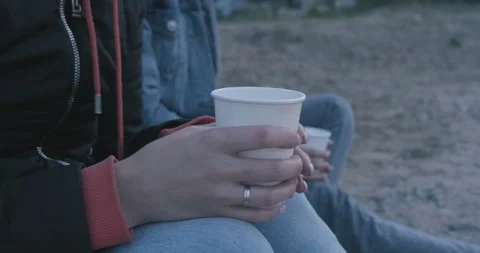 Close-up of Paper White Cup in Hands of Young Girl. Woman Sits on Sandy Beach Stock Footage 134382929
