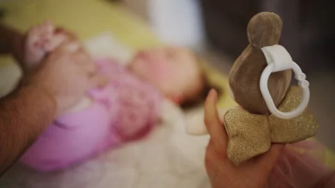 Close up of a parent holding a soft plush toy with a ring near a baby lying down Stock Footage 335526543