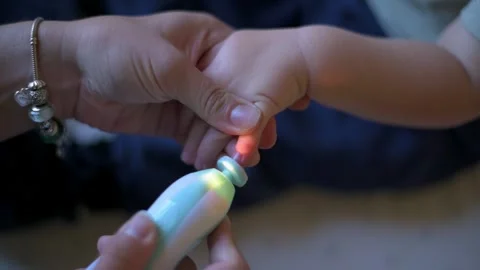 Close-up of parent using glowing electric nail file to trim toddler fingernails Video stock 295838660