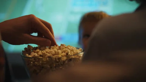 Close-up of parents hands taking popcorn out of a bowl while watching a movi Stock Footage 305338661